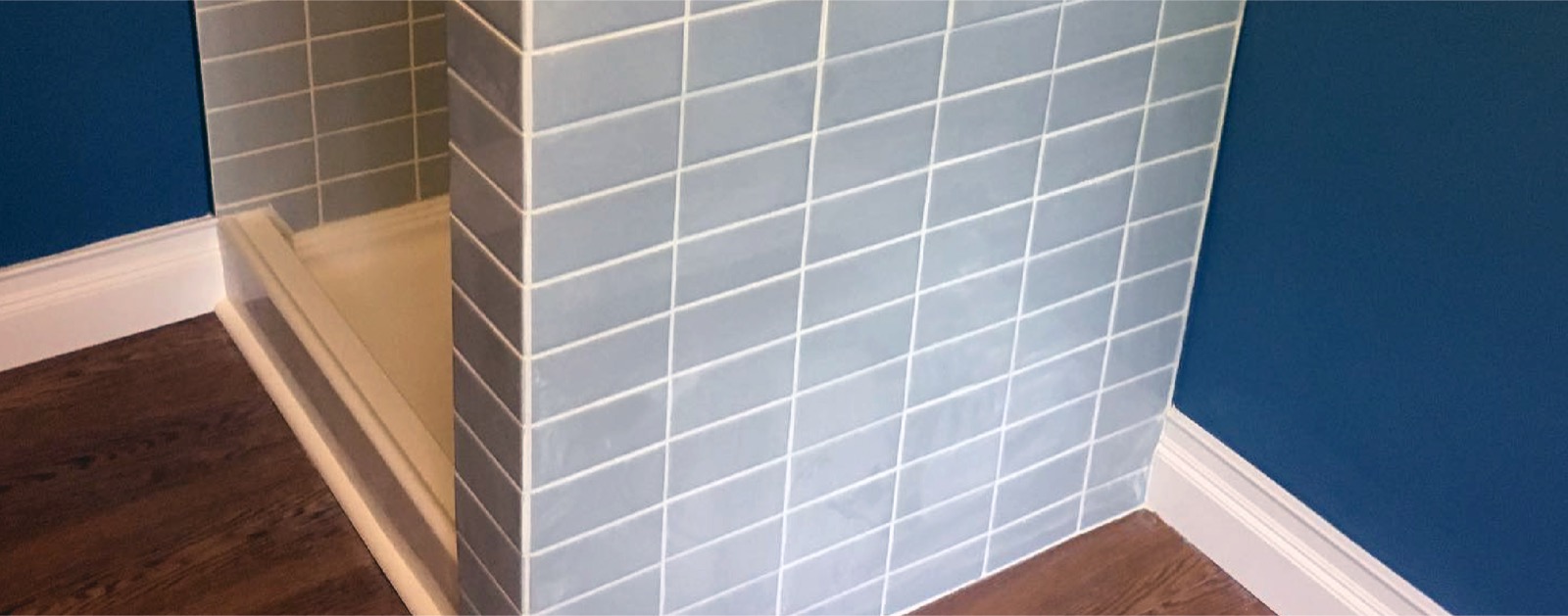 A finished bathroom by AV General Contracting — subway-tile shower, hardwood floor and clean baseboards.